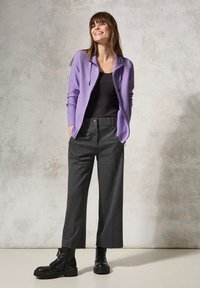 Sweat à zip violet, débardeur noir, pantalons larges gris et bottes noires à lacets. Texture lisse, coupe décontractée et couleurs contrastées.