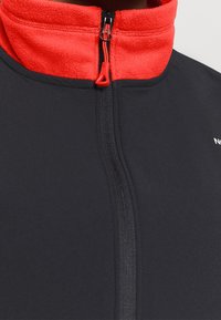 Giacca in pile con zip e colletto alto. Il colore principale è grigio scuro, con colletto interno rosso. Dotata di una zip centrale e di un logo.