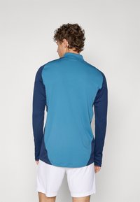 Long-sleeve polo shirt in a mix of light blue and navy blue. Features a collared neckline and textured fabric. Tailored fit with side accents.