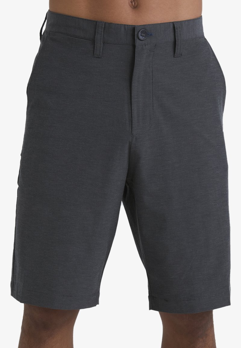 Pantalones cortos de color gris oscuro, hechos de tela ligera, con un corte frontal plano, cierre de botón y bolsillos laterales. Textura suave con un diseño minimalista.