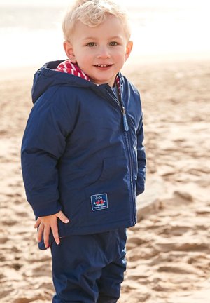 Giacca piumino blu navy con cappuccio, caratterizzata da una fodera a scacchi rossi e bianchi. Include una cerniera frontale e un logo a patch sulla tasca.