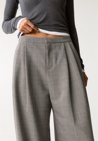 Pantalon gris à carreaux avec plis, en tissu léger et lignes roses subtiles. Coupe ample avec une ceinture lisse.
