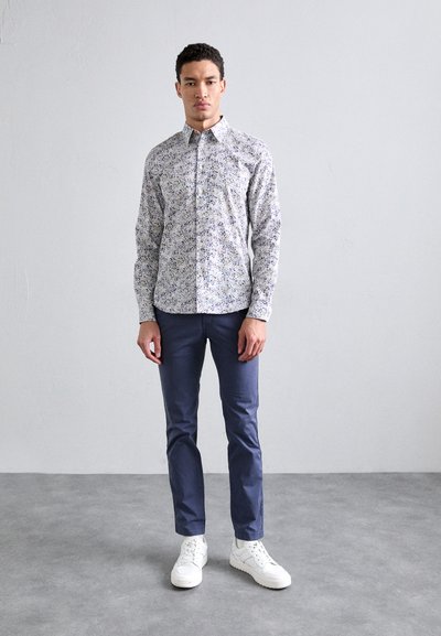 Long-sleeve shirt with a multicolored floral pattern, button-up design, paired with navy trousers and white sneakers, standing on a gray surface.