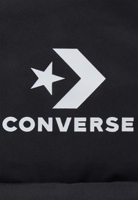 Un tissu noir avec un grand logo blanc arborant une étoile et une flèche, accompagné du mot "CONVERSE" en lettres blanches en gras.