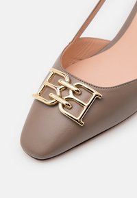 Chaussure plate en cuir couleur taupe avec bout carré et détail de boucle entrelacée dorée à l'avant.