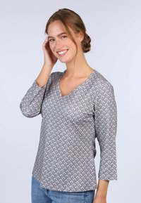 Grau gemusterte Bluse mit Dreiviertelärmel, V-Ausschnitt, die ein sich wiederholendes Motiv in Rosa und Weiß zeigt. Weicher Stoff mit lockerem Schnitt.