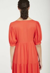 Červené, pruhované šaty po kolena s krátkými nabíranými rukávy a volánkovou sukní. Hladká textura, uvolněný střih a široký výstřih.