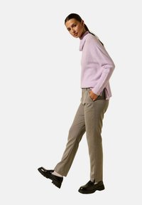 Pull en lilas tricoté avec un col montant, associé à un pantalon gris clair et des chaussures noires. Le pull présente une coupe décontractée et des fentes sur les côtés.