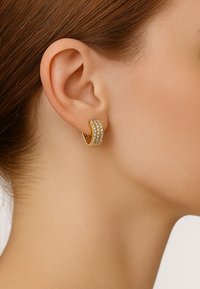 Goldene Creolen mit zwei Reihen klarer Strasssteine, ausgestattet mit einer glatten Oberfläche und polierter Textur, die am Ohr eines Models befestigt sind.