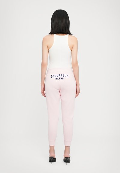 Balta bezcilvēka topa kombinācija ar gaiši rozā sporta biksēm, kurām aizmugurē ir uzraksts "DSQUARED2 MILANO" tumši zilā krāsā; pieguļošs piegriezums, mīksta auduma un ribota aproces.