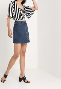 Top de manga corta a rayas en blanco y negro combinado con una falda de mezclilla azul con cierre de botones en el frente y dobladillo deshilachado. Usado con sandalias de tacón cuadrado negras.