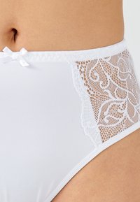 Hoge taille witte onderbroeken van soepele stof met een kantpaneel met bloemenpatronen aan de zijkant, versierd met een klein strikje.