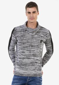 Gestrickter grauer und schwarzer Pullover mit hohem Kragen, strukturierten schwarzen Seitenelementen und Kordelzügen, hergestellt aus einem weichen Material.