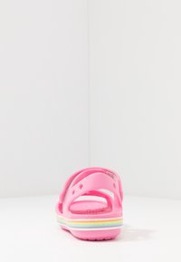 Vaaleanpunaiset sandaalit, joissa on teksturoitu pohja, avoin kanta ja kaksi säädettävää hihnaa. Iloiset sateenkaaren väriset korostukset pohjassa lisäävät muotoilua.