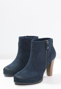 Bottes chelsea marine en suédine, avec une fermeture éclair sur le côté et un talon haut texturé. Bout arrondi et col légèrement rembourré.