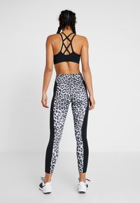 Soutien-gorge de sport noir avec un design croisé au dos ; legging taille haute avec un motif léopard et des panneaux latéraux noirs.