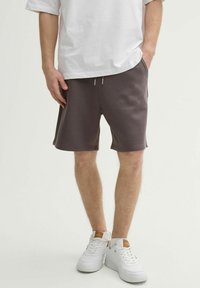 Pantalones cortos de algodón gris con cintura ajustable, bolsillos laterales y un corte relajado, combinados con zapatillas blancas y una camiseta blanca holgada.