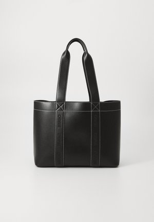 Sac fourre-tout en cuir noir avec doubles poignées et coutures blanches visibles, debout sur un fond clair uni.