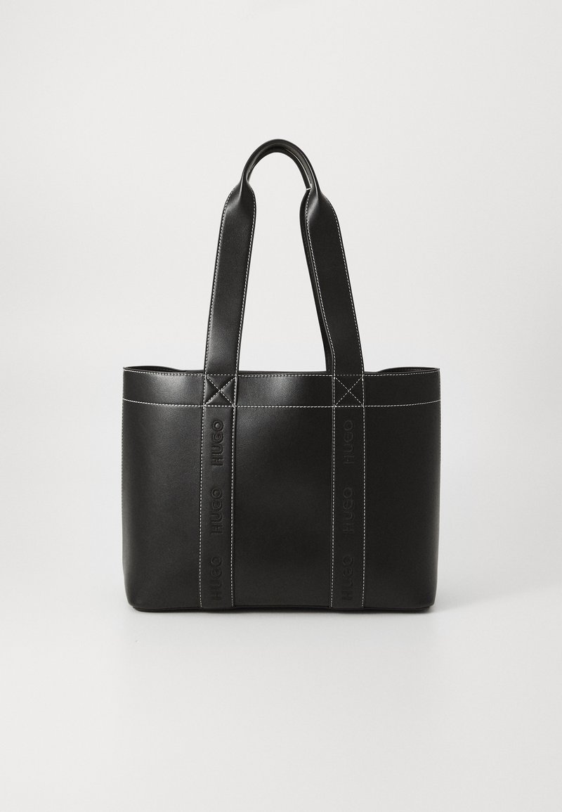 Sac fourre-tout en cuir noir avec doubles poignées et coutures blanches visibles, debout sur un fond clair uni.