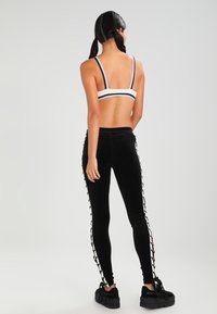 Svarta sammetstights med sidodetaljer i snörning, ihopparade med en vit och marinblå randig bralette. Slät textur, tight passform.