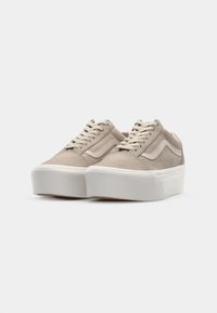 Beige semskinn-sneakers med en tykk hvit plattformsåle, flate beige snører og laterale striper i en matchende nyanse.