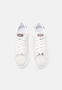 Ζευγάρι εκρού σουέτ αθλητικά παπούτσια με άσπρα κορδόνια, μπορντό πίσω τμήματα και λογότυπο "Steve Madden" στη γλώσσα και στην ετικέτα των κορδονιών.