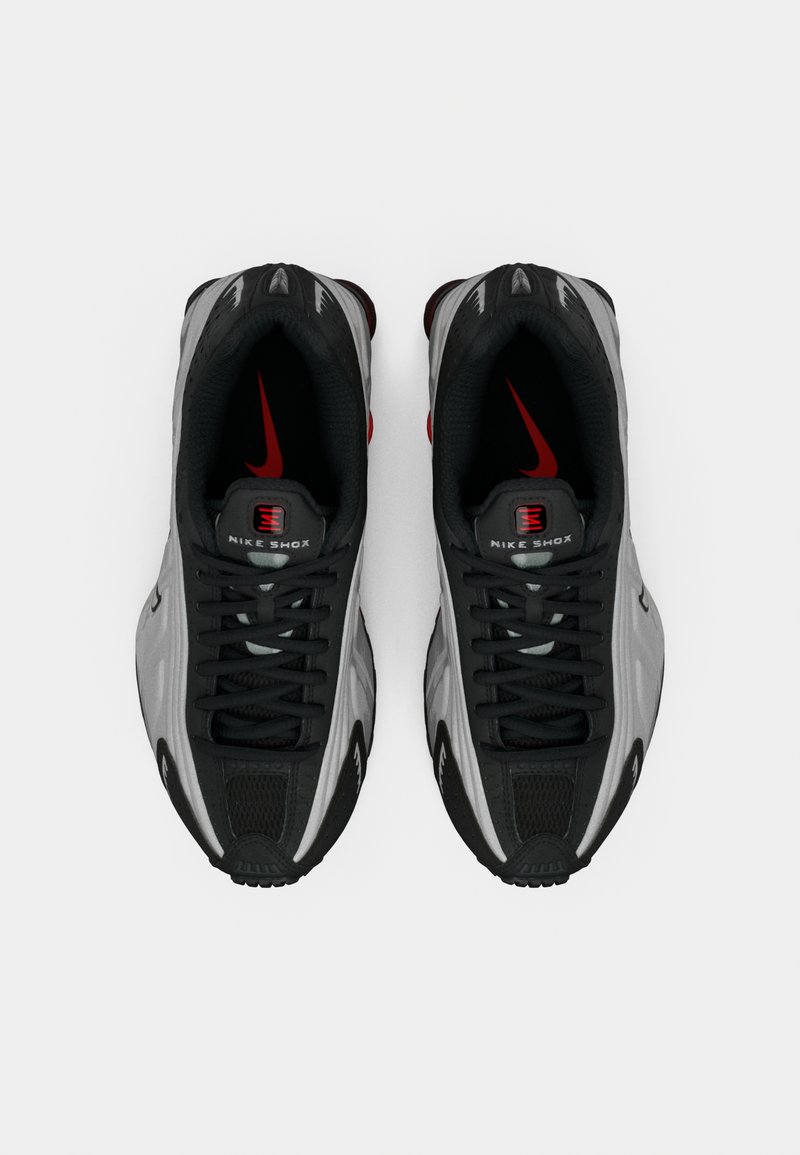 Une paire de baskets Nike Shox noires et grises avec des accents de logo rouges, vue de dessus sur un fond blanc.