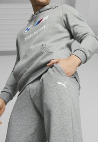 Grå hoodie med BMW Motorsport-logotyp och vit Puma-logotyp på matchande byxor. Har en känguruficka och ribbade muddar. Mjuk textur.