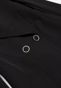 Černá bunda s upraveným střihem, vybavená dvěma kulatými stříbrnými knoflíky a hladkými sklady. Vyrobena z hladkého materiálu s matnou texturou.