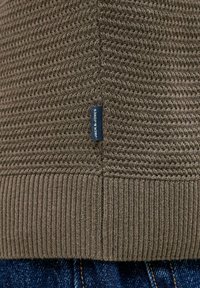 Pull en maille vert olive texturé avec ourlet côtelé et étiquette foncée. Présente un tissage lisse et un motif structuré.