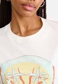 Crème-kleurig t-shirt met een ronde halslijn, voorzien van een versleten grafisch ontwerp van palmbomen en "ENDLESS SUMMER" in pastelkleuren.