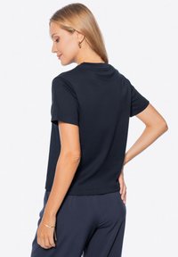 T-shirt in cotone blu navy con maniche corte e scollatura rotonda, caratterizzata da una vestibilità comoda e una texture liscia, indossata con pantaloni scuri.