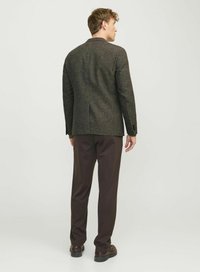 Veste en tweed marron avec un design structuré, une seule fente et des poignets boutonnés, assortie à un pantalon et des chaussures marron foncé.