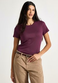 T-shirt aderente color bordeaux con trama a coste e scollo rotondo, abbinata a pantaloni beige a gamba larga e cintura marrone.