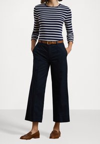 Randig långärmad topp i marinblått och vitt, tillsammans med löst sittande marinblå byxor. En brun bälte med metallspänne och bruna loafers fulländar looken.