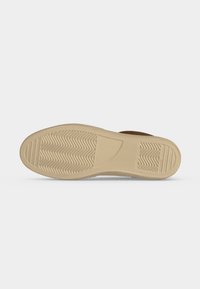 Semelle de chaussure avec motif en caoutchouc beige présentant des motifs en zigzag et linéaires pour l'adhérence, affichée sur un fond uni gris clair.