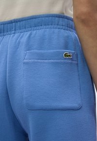 Ανοιχτό μπλε παντελόνι φόρμας με υφασμάτινη υφή, ελαστική μέση και πίσω τσέπη που διαθέτει ένα μικρό πράσινο λογότυπο κροκόδειλου.