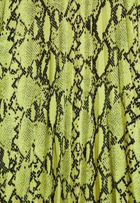 Tissu vert citron avec un imprimé serpent texturé en noir, présentant un motif de diamants et d'écailles, disposé en plis verticaux.