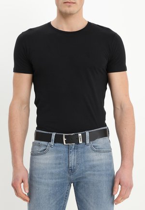T-shirt noir à manches courtes avec une coupe ajustée, associé à un jean bleu délavé et une ceinture noire brillante présentant une boucle en argent et une étiquette de logo.