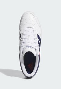 Białe sneakersy z skórzaną cholewką, granatowymi paskami, czerwonym akcentem i perforowanym noskiem. Standardowe sznurowadła i wyściełany kołnierz dla komfortu.