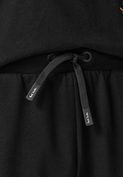 Ceinture de pantalon de jogging noire avec cordon de serrage noir attaché portant l'inscription « Paul Smith » sur les extrémités.