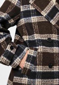 Geruite wol coat in bruin, marineblauw en crème. Voorzien van een notch-kraag en zwarte knopen. Zachte textuur met een iets oversized pasvorm.
