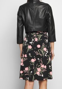 Černá kožená zkrácená bunda přes šaty s květinovým vzorem, které mají růžové květy a zelené listy na černém pozadí. Hladká textura, přiléhavý střih.