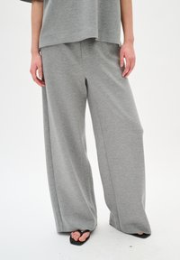 Pantaloni della tuta grigi a gamba larga realizzati in un tessuto morbido. Presentano una vestibilità rilassata senza motivi prominenti, abbinati a semplici sandali neri.