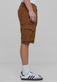 Brune cargo shorts laget av bomull med sidelommer, brettet hem og avslappet passform. Kombinert med hvite sneakers og ankelsokker.