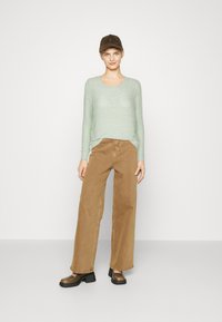 Maglione lavorato a maglia verde menta, pantaloni larghi color beige e berretto marrone scuro con visiera piatta. Scarpe platform nere con punta arrotondata.