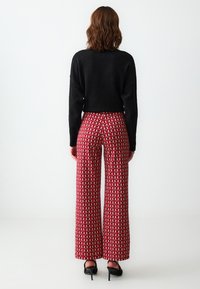 Pantaloni larghi a righe rosse con un design geometrico, abbinati a un maglione nero a maniche corte. Tessuto morbido e vestibilità rilassata.