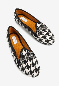 Czarno-białe baleriny w wzór houndstooth z teksturowanej tkaniny, pomarańczowe, puszyste wnętrze i dekoracyjny detal łańcuszka z przodu.