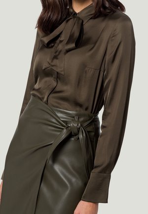 Donkergroene zijden blouse met een strik bij de kraag, gecombineerd met een leren rok met hoge taille en een knoopdetail.