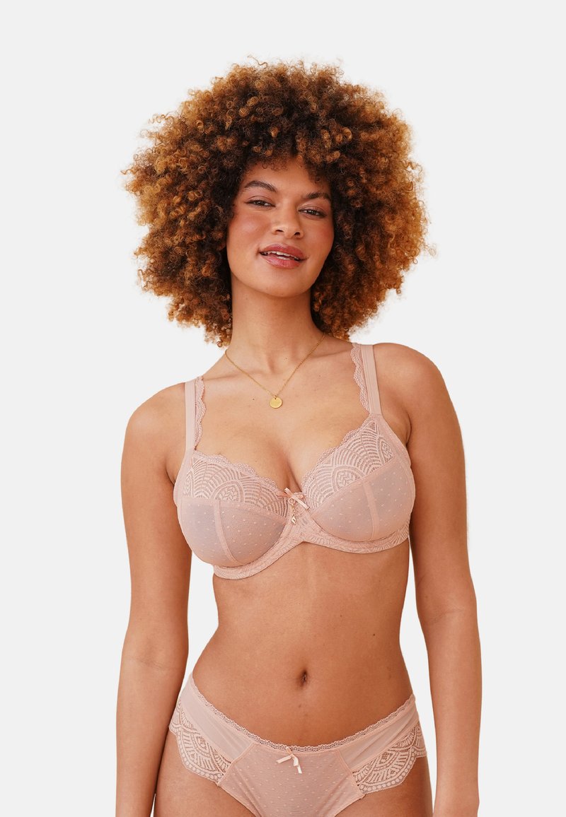 Bra and panty set in soft nude fabric, featuring lace trim, polka dot texture, and intricate geometric patterns, with a central bow accent.